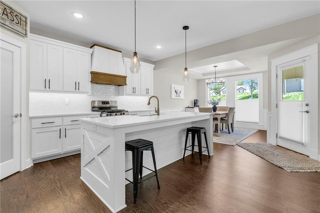 kitchen with stainless steel gas range, a breakfast bar, dark wood-type flooring, a center island with sink, and light countertops