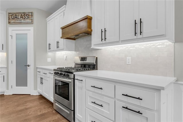 kitchen featuring stainless steel gas range oven, light wood-type flooring, light countertops, and tasteful backsplash