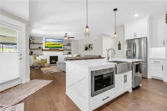 kitchen featuring a sink, appliances with stainless steel finishes, a ceiling fan, a warm lit fireplace, and dark wood finished floors