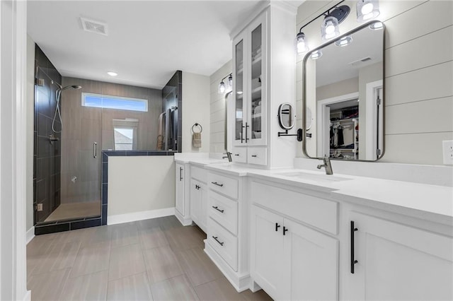 bathroom with a shower stall, double vanity, a spacious closet, and baseboards