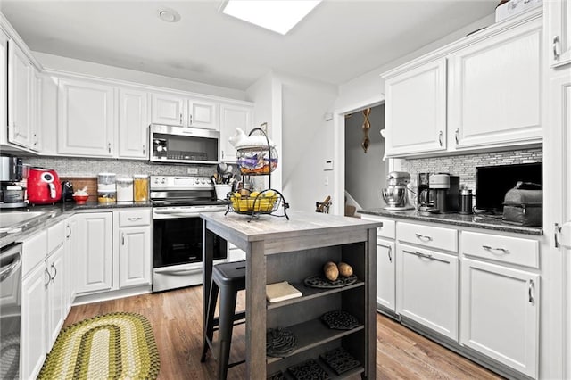 kitchen featuring stainless steel appliances, tasteful backsplash, white cabinetry, dark countertops, and light wood finished floors