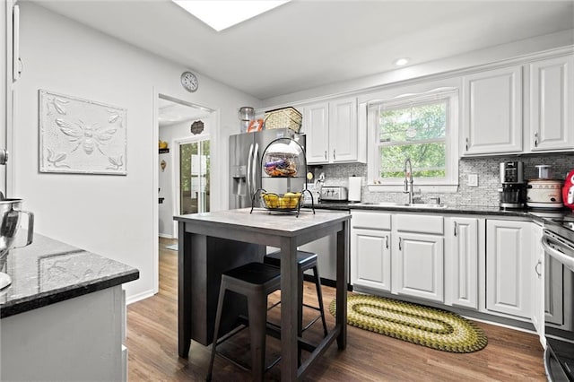 kitchen with stainless steel appliances, a sink, white cabinetry, decorative backsplash, and wood finished floors