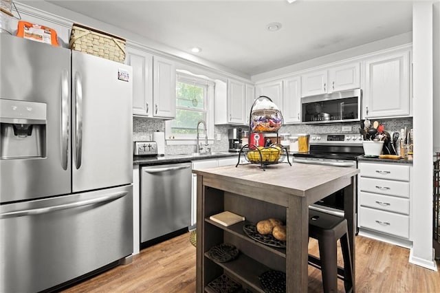 kitchen featuring appliances with stainless steel finishes, a sink, light wood finished floors, white cabinets, and recessed lighting