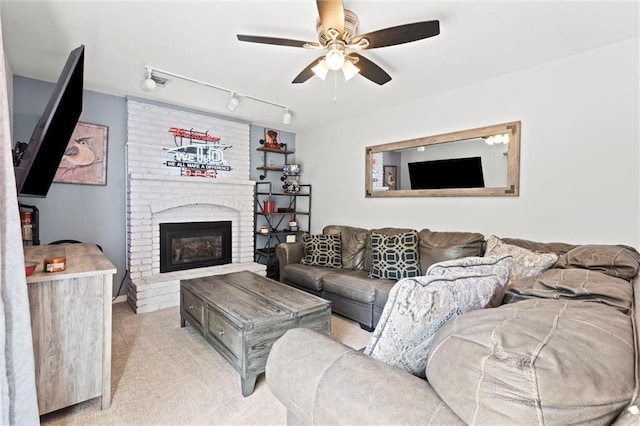 living room with light carpet, ceiling fan, rail lighting, and a brick fireplace