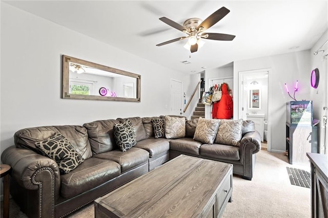 living area with stairs, light carpet, and a ceiling fan