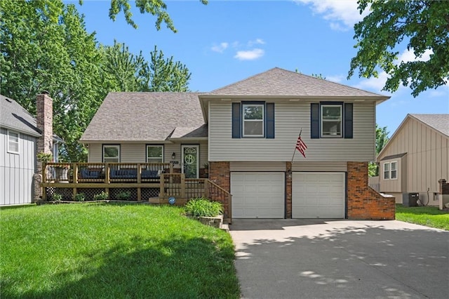 tri-level home featuring an attached garage, brick siding, a front lawn, driveway, and a wooden deck