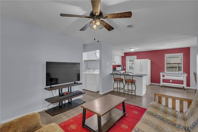 living room featuring washing machine and dryer, ceiling fan, wood finished floors, and baseboards