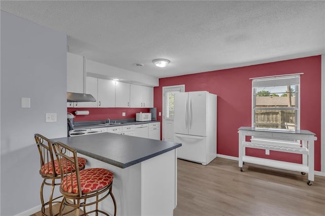 kitchen featuring white appliances, dark countertops, a textured ceiling, a peninsula, and light wood-style floors