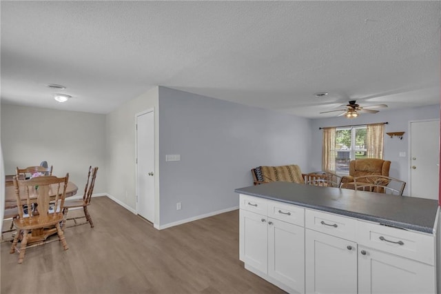 kitchen featuring a textured ceiling, light wood-style flooring, dark countertops, white cabinetry, and ceiling fan