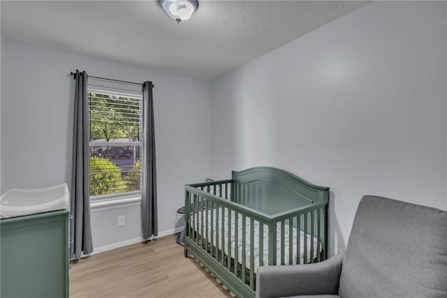 bedroom with light wood finished floors, a textured ceiling, and baseboards