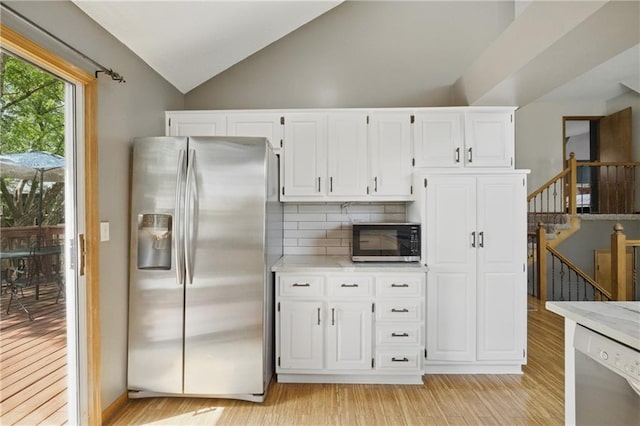 kitchen featuring stainless steel refrigerator with ice dispenser, black microwave, dishwasher, light countertops, and vaulted ceiling