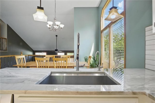 kitchen with a sink, light stone countertops, a chandelier, and pendant lighting
