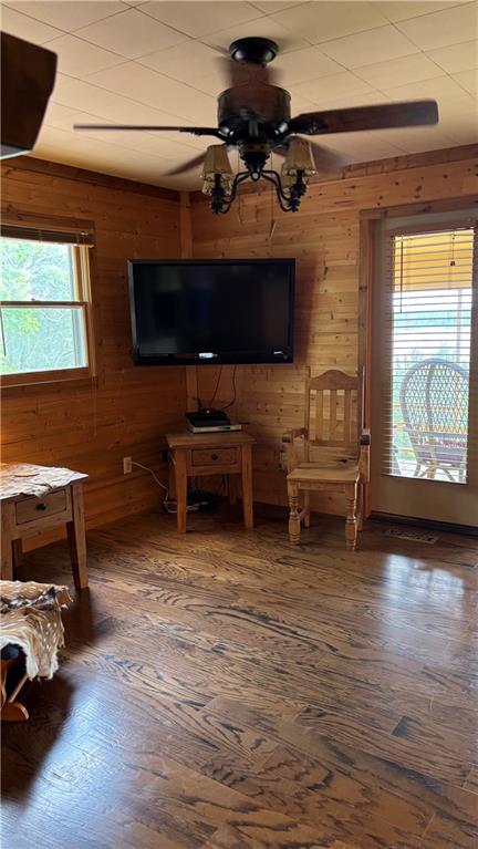 unfurnished living room featuring wooden walls, hardwood / wood-style flooring, and ceiling fan
