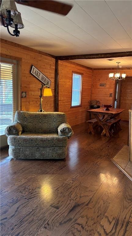 living area featuring wooden walls, a chandelier, wood finished floors, and beam ceiling