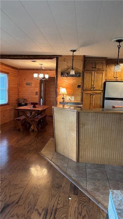 kitchen with freestanding refrigerator, wooden walls, wood finished floors, a chandelier, and brown cabinetry