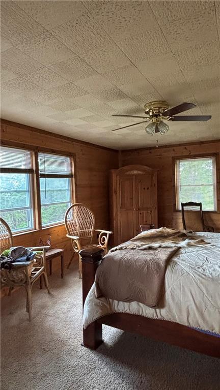 bedroom with multiple windows, wood walls, carpet floors, and ceiling fan