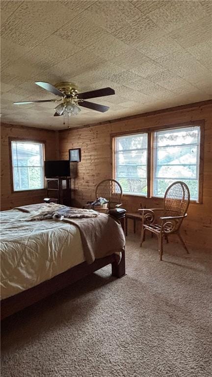 carpeted bedroom with wooden walls, multiple windows, and ceiling fan