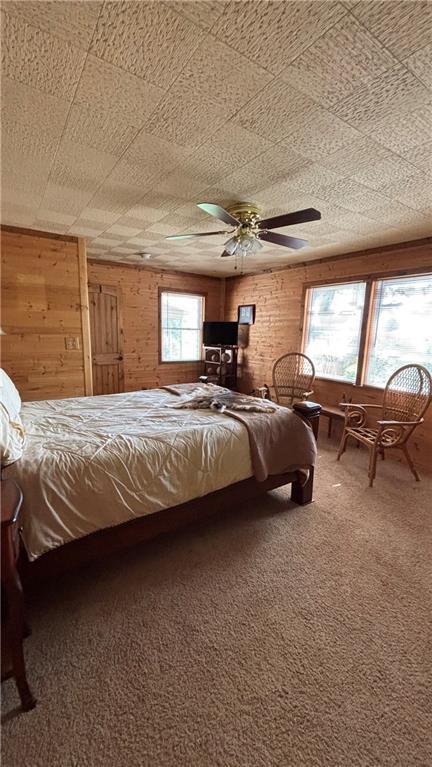 bedroom with wood walls, carpet floors, and ceiling fan