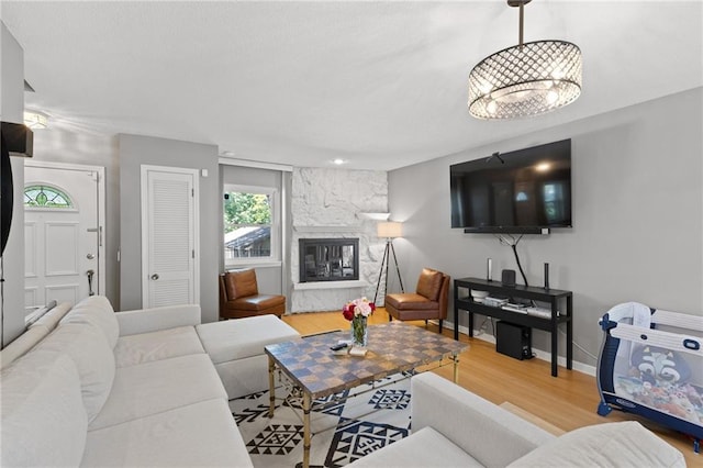 living area featuring wood finished floors, a stone fireplace, and baseboards