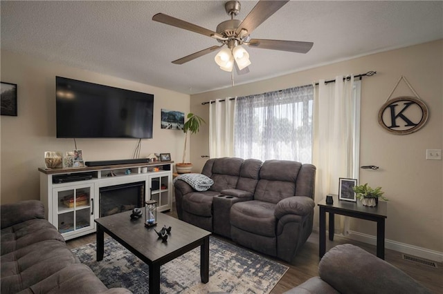 living room featuring a ceiling fan, wood finished floors, baseboards, and a textured ceiling