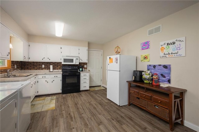 kitchen with white appliances, a sink, wood finished floors, independent washer and dryer, and white cabinetry