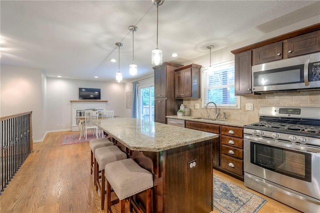 9711 Roe Ave, Overland Park, KS 66207 - kitchen with appliances with stainless steel finishes, a center island, a kitchen breakfast bar, light stone countertops, and light wood-type flooring