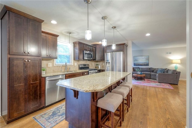 9711 Roe Ave, Overland Park, KS 66207 - kitchen featuring stainless steel appliances, a breakfast bar, light wood finished floors, decorative backsplash, and a kitchen island