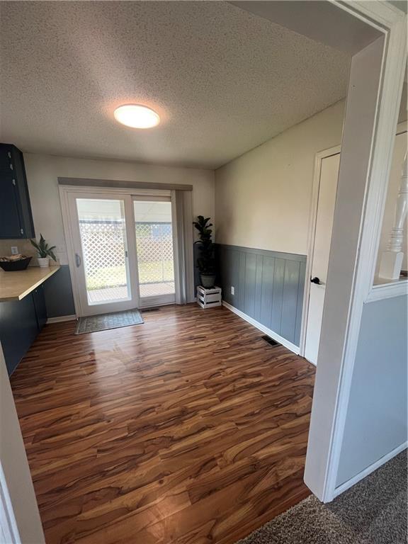 1424 S Olive St, Ottawa, KS 66067 - unfurnished dining area with a textured ceiling, dark wood-style floors, and wainscoting