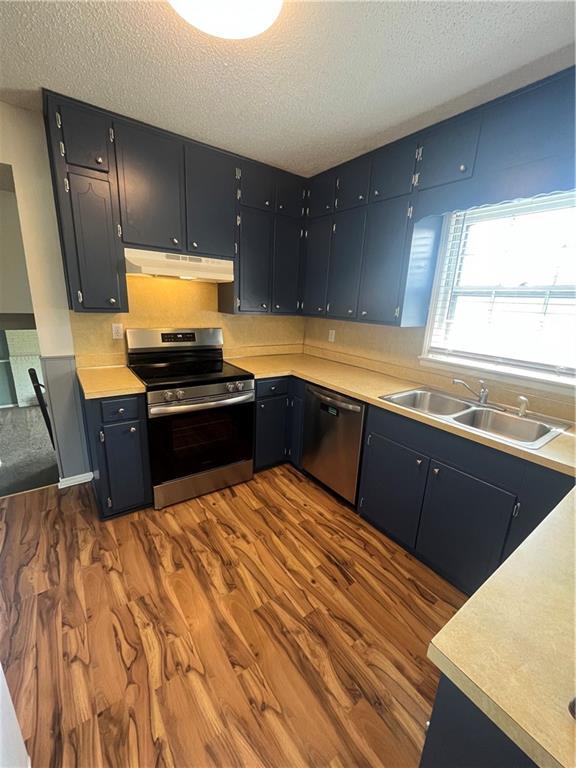 1424 S Olive St, Ottawa, KS 66067 - kitchen featuring stainless steel appliances, under cabinet range hood, a textured ceiling, dark wood-style flooring, and light countertops