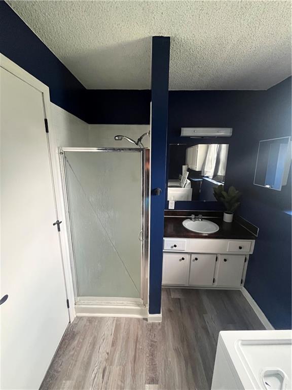 1424 S Olive St, Ottawa, KS 66067 - bathroom featuring a textured ceiling, wood finished floors, vanity, and a shower stall