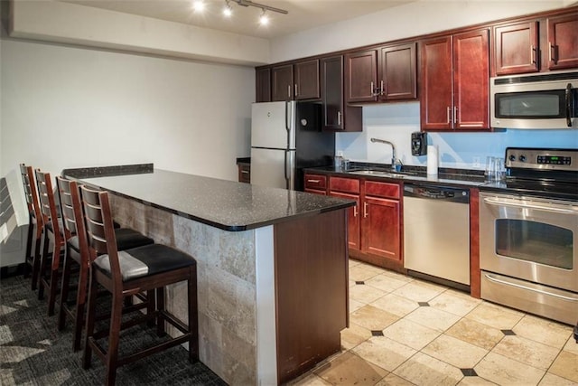 700 E 8th St Unit 10J, Kansas City, MO 64106 - kitchen with stainless steel appliances, a sink, reddish brown cabinets, a breakfast bar, and track lighting