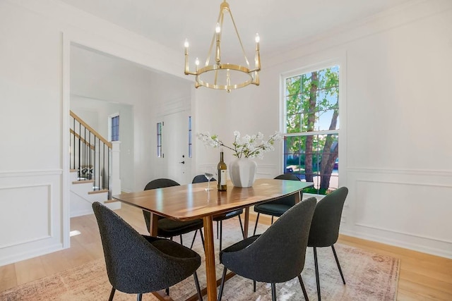 dining room with a decorative wall, a chandelier, stairs, light wood-style flooring, and a wainscoted wall