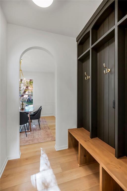 mudroom featuring arched walkways, light wood finished floors, and baseboards