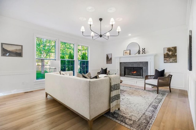 living room with a chandelier, a tile fireplace, light wood-style floors, a decorative wall, and crown molding