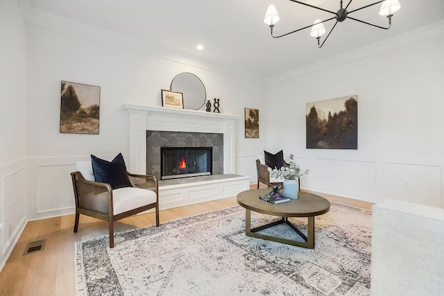 living room with wood finished floors, a chandelier, crown molding, a fireplace, and a decorative wall