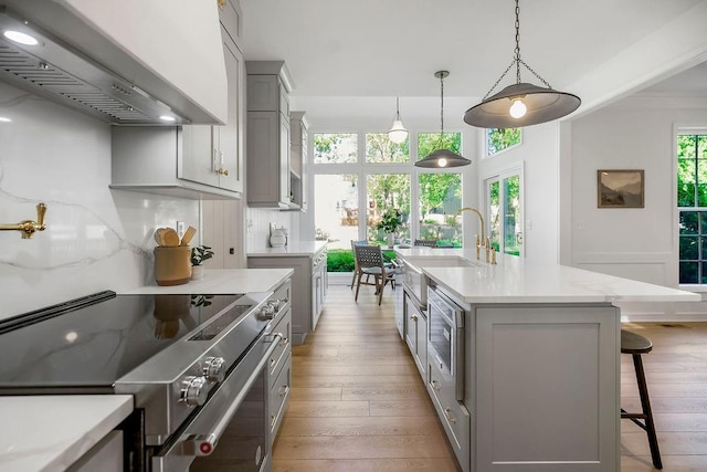 kitchen featuring wall chimney exhaust hood, range with electric cooktop, a sink, gray cabinets, and light wood-type flooring