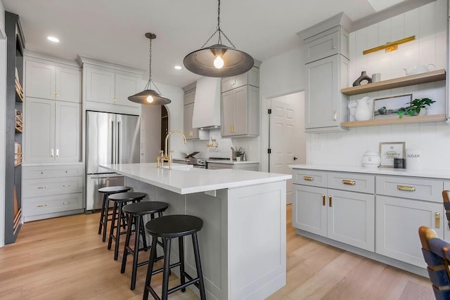 kitchen featuring high end refrigerator, a sink, custom range hood, open shelves, and light countertops
