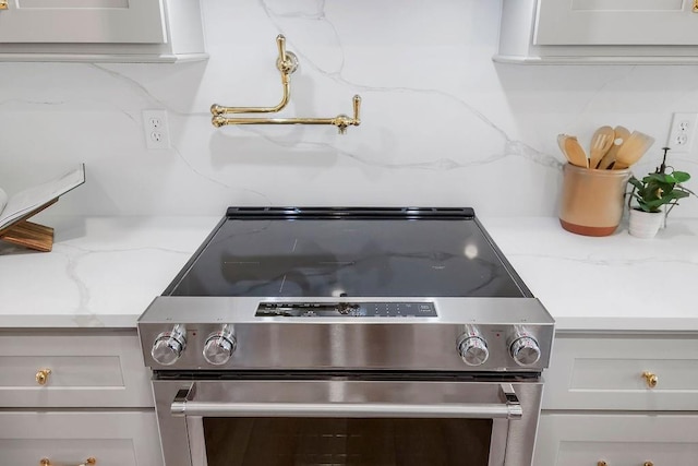 detailed view of stainless steel range with electric cooktop, tasteful backsplash, and light stone counters