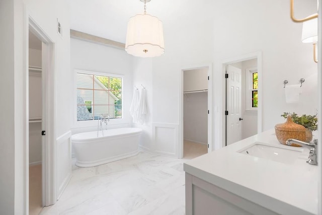 bathroom with a walk in closet, a soaking tub, vanity, wainscoting, and a decorative wall