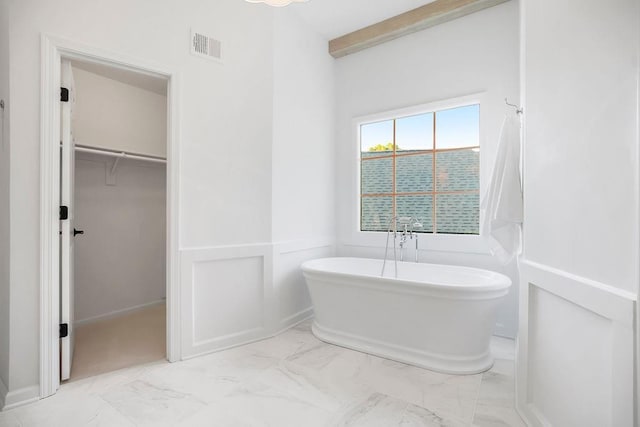 full bathroom with marble look tiles, a freestanding bath, a spacious closet, and beamed ceiling