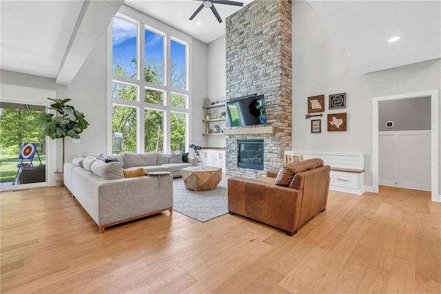living room with a high ceiling, a ceiling fan, a fireplace, and light wood finished floors