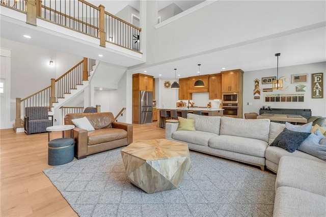 living area with light wood-type flooring, stairway, a high ceiling, and recessed lighting