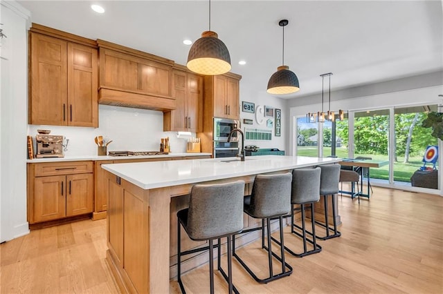 kitchen featuring stainless steel appliances, light countertops, light wood-style floors, an island with sink, and recessed lighting