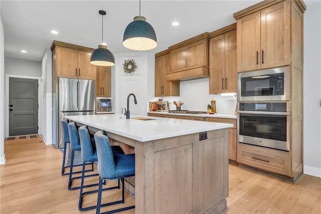 kitchen with appliances with stainless steel finishes, a sink, backsplash, a breakfast bar, and light countertops