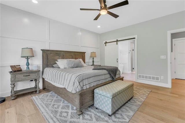 bedroom with a barn door, light wood-type flooring, recessed lighting, a ceiling fan, and baseboards