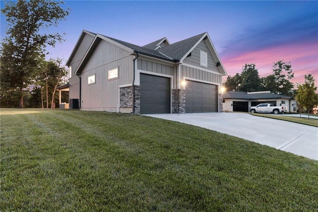 property exterior at dusk with board and batten siding, a yard, driveway, and stone siding
