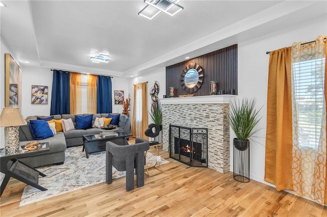 living room featuring a raised ceiling, wood finished floors, a fireplace, and recessed lighting