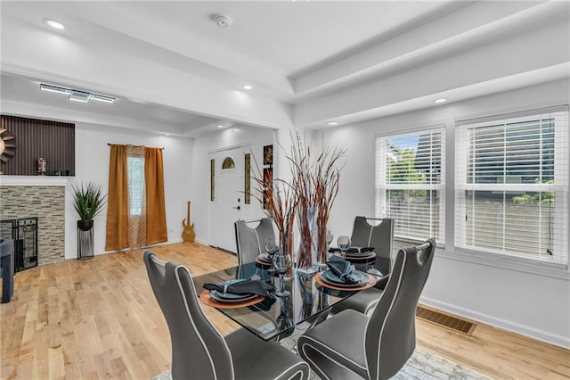 dining area featuring light wood-type flooring, a tray ceiling, baseboards, a fireplace, and recessed lighting