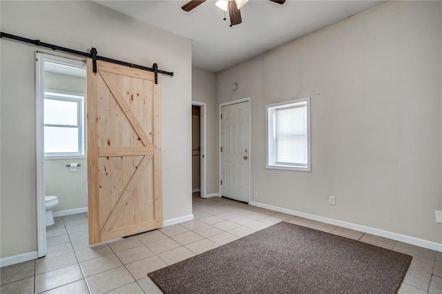 spare room featuring a barn door, light tile patterned flooring, a ceiling fan, and baseboards