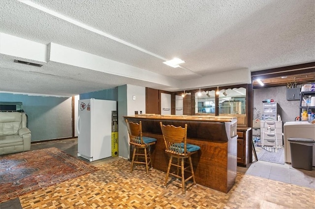 613 NE 90th Ter, Kansas City, MO 64155 - kitchen with freestanding refrigerator, a textured ceiling, and a breakfast bar area